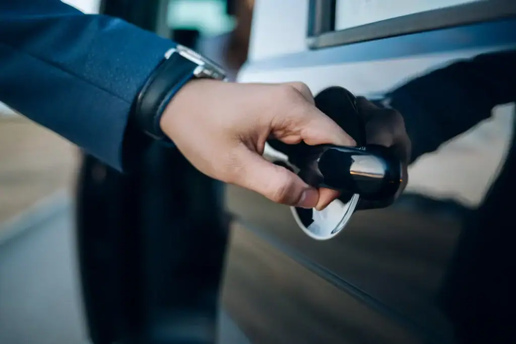 A close-up of a person’s hand wearing a blue suit opening a car door by pulling the handle, with the reflection of the hand visible on the car's shiny surface. The scene, likely captured outside a luxury venue in Atlantic City, NJ, suggests a moment of professional service or arrival at a high-end destination.